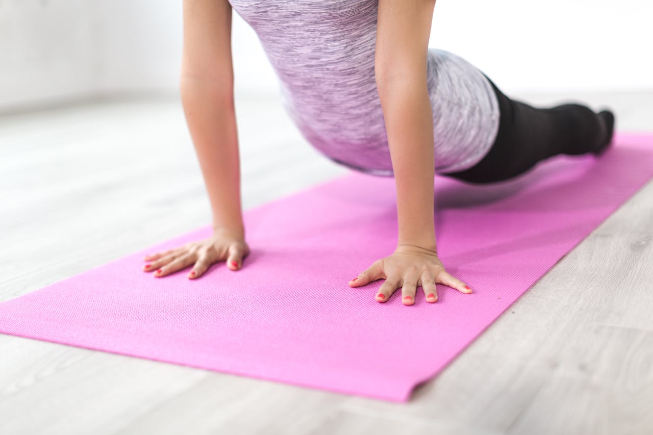 gallery-02 A woman performs a yoga stretch indoors on a pink mat, promoting a healthy lifestyle.