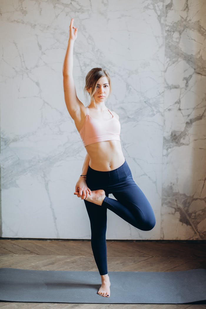 Young woman doing yoga pose on mat in bright indoor space, promoting wellness.